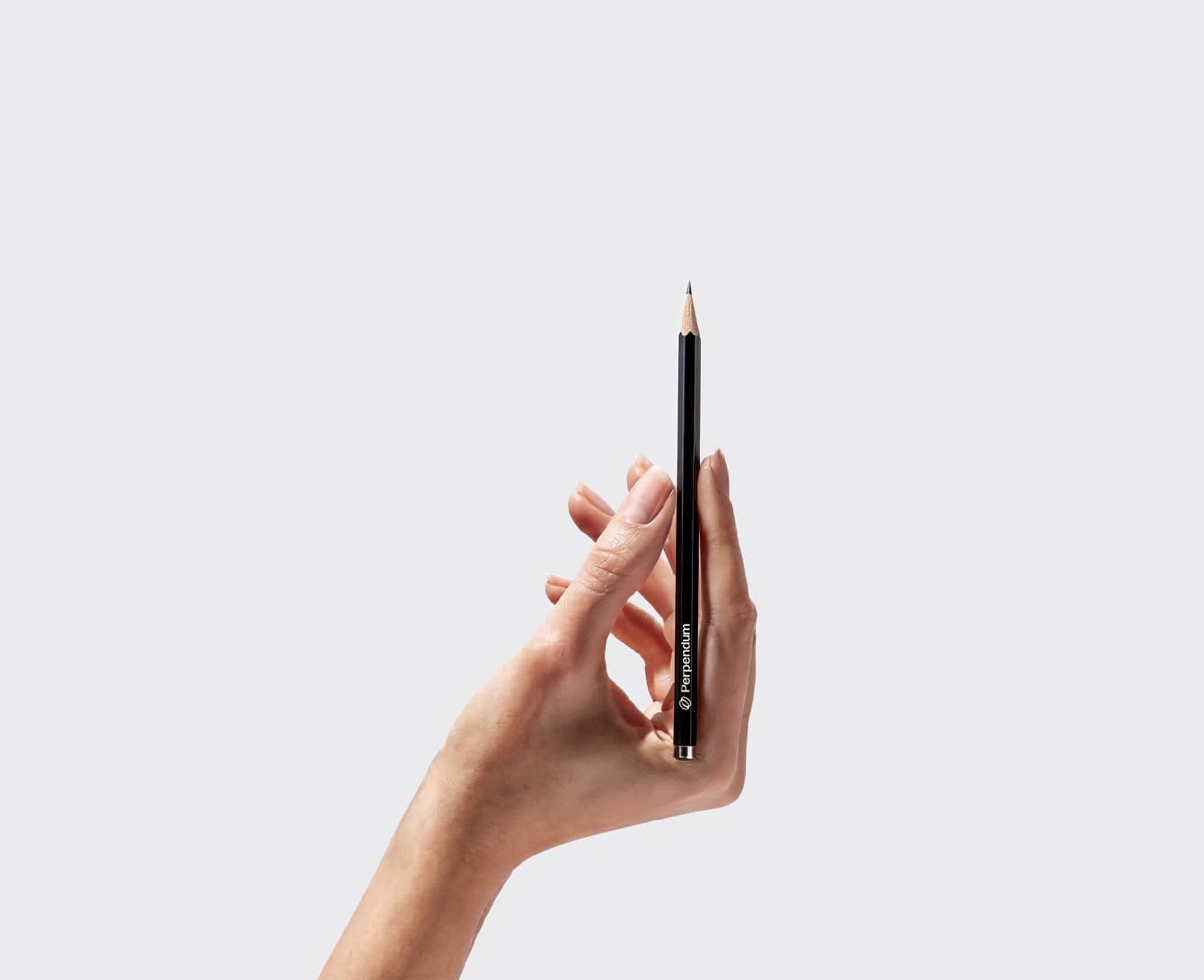 A hand holding a black Perpendum pencil upright against a pale grey ground.